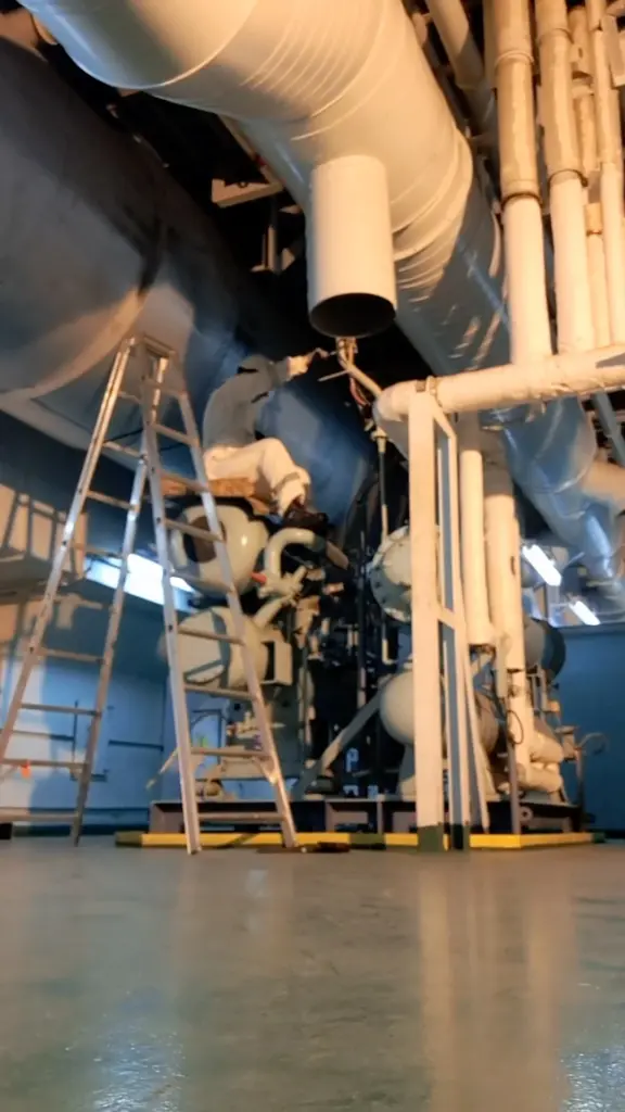 Engineer working on overhead machinery and pipework in an engine room