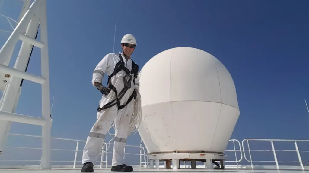 Elektrohertz founder in coveralls and safety harness on the deck of a merchant vessel beside a satellite communications dome