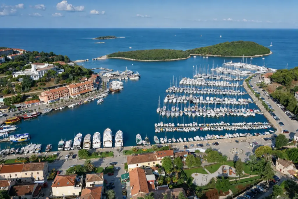 Veduta aerea della Marina Vrsar a Orsera, imbarcazioni ormeggiate di poppa lungo i pontili con il paese e le isole alle spalle